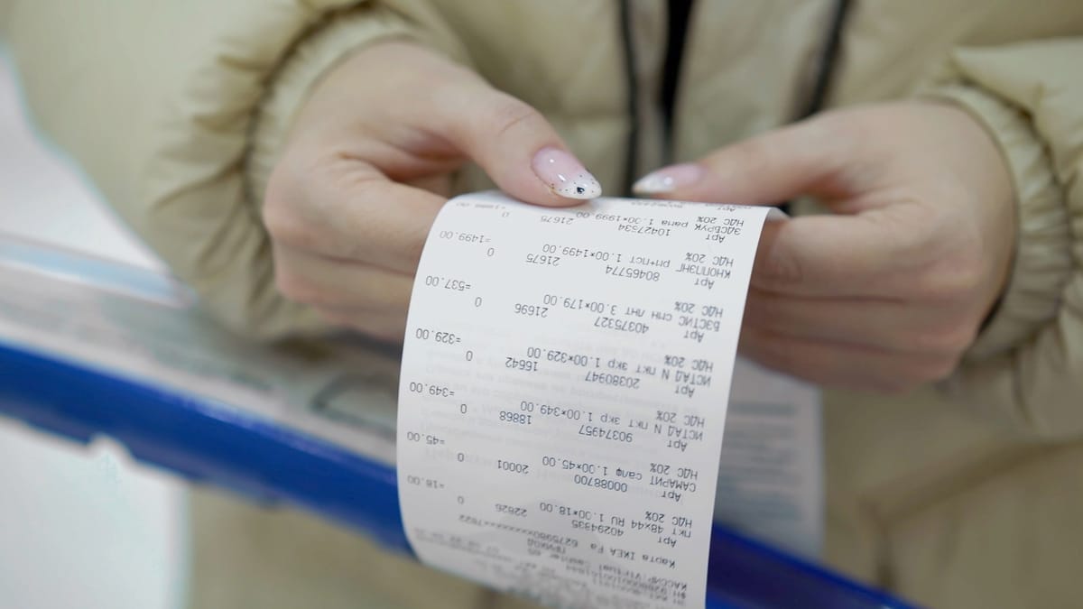 Hands unrolling a long paper till receipt printed with itemised lines and VAT